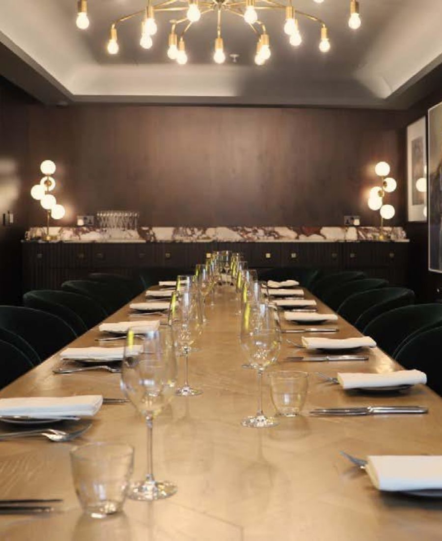 Event space long table setup with wine glasses, green velvet chairs, golden pendant lights and dark wood accent wall