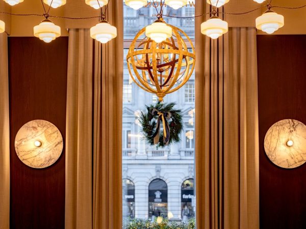 The interior of Wild Honey St James dressed for Christmas Eve, with a festive wreath in the window, golden globe chandelier and warm ambient lighting overlooking Pall Mall