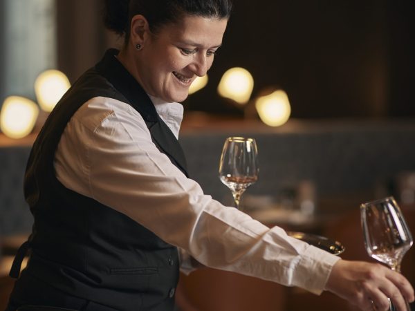 Restaurant staff member pouring wine at table with ambient lighting in background