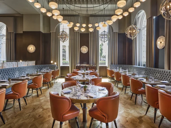 Wild Honey St James main dining room with orange leather chairs, blue tufted banquettes, geometric sphere chandeliers and large windows