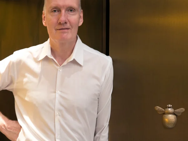 Chef Anthony Demetre portrait in white shirt standing confidently at Wild Honey restaurant with golden bee sculpture