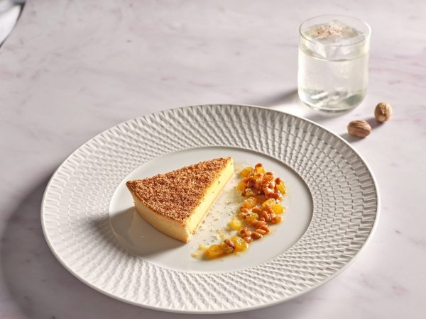 Elegant dessert dish with golden caramelized top served with fruit compote and nuts on textured white plate at Wild Honey